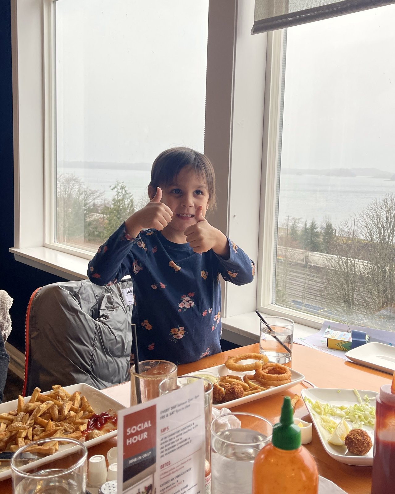 Young guest giving thumbs up at the ocean-view window seat, OV Burger Bar Prince Rupert